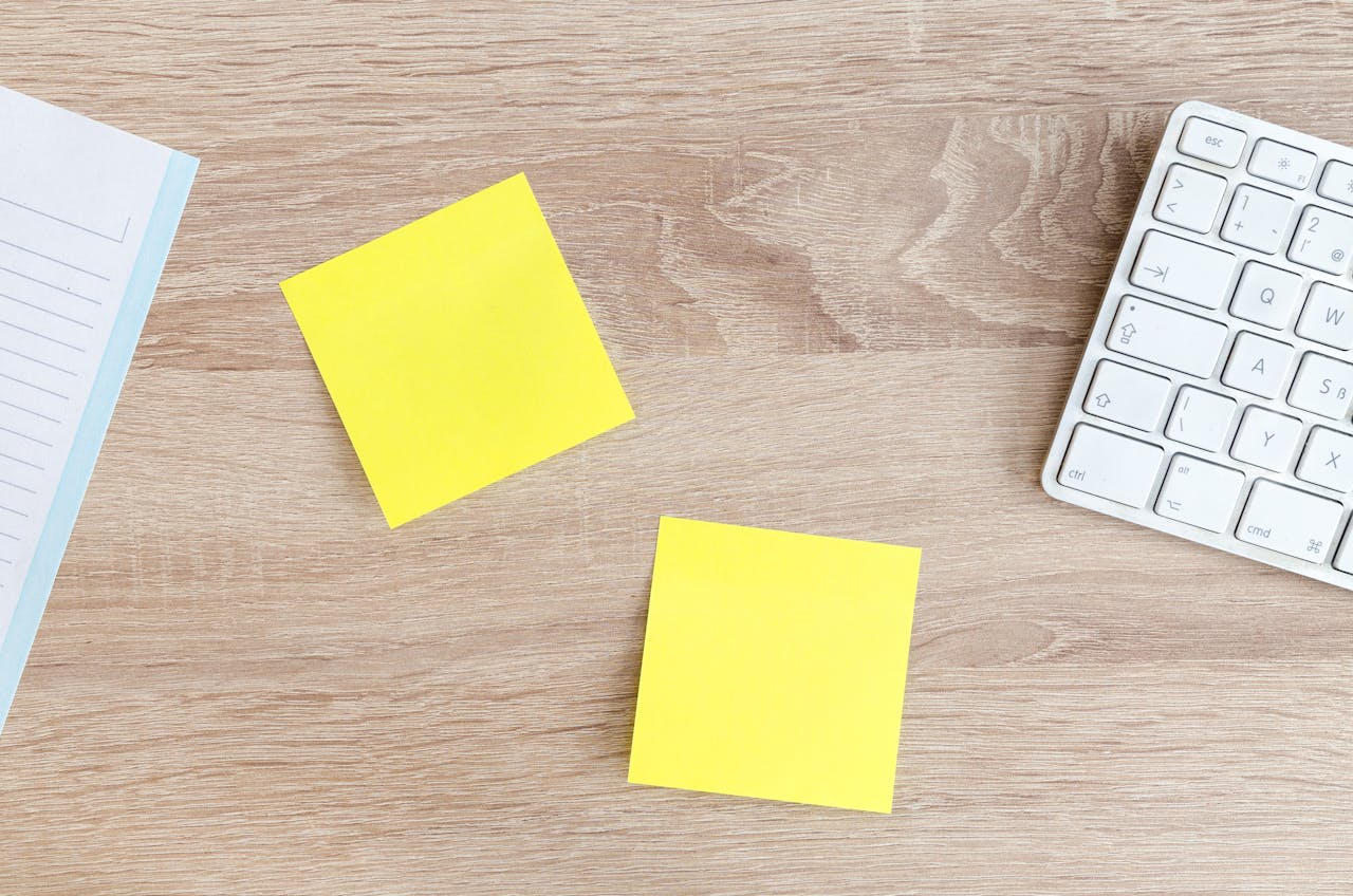 Home Flat lay of a workspace featuring yellow sticky notes, a keyboard, and a notebook on a wooden desk.